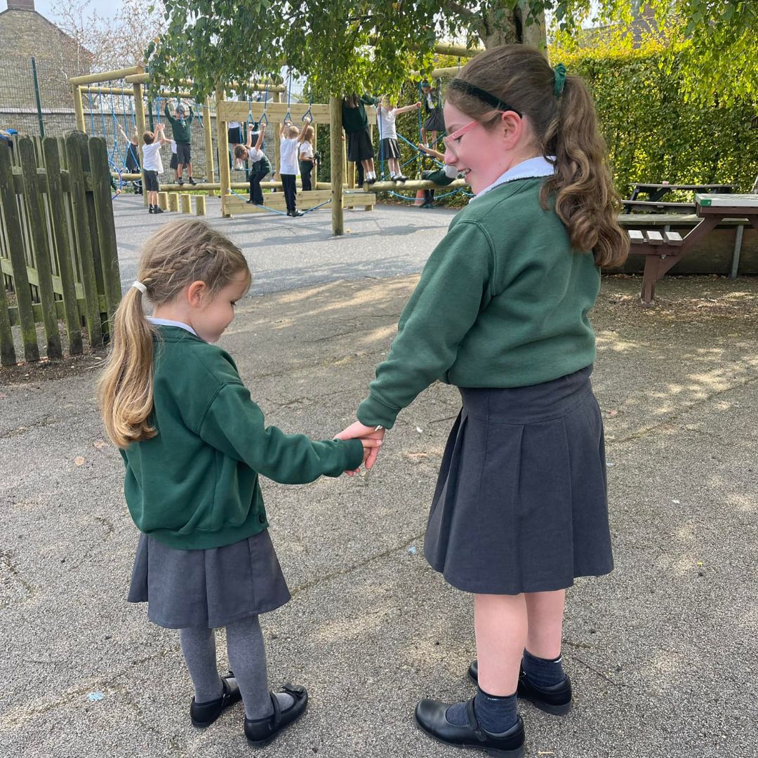 A year 6 and reception pupil holding hands